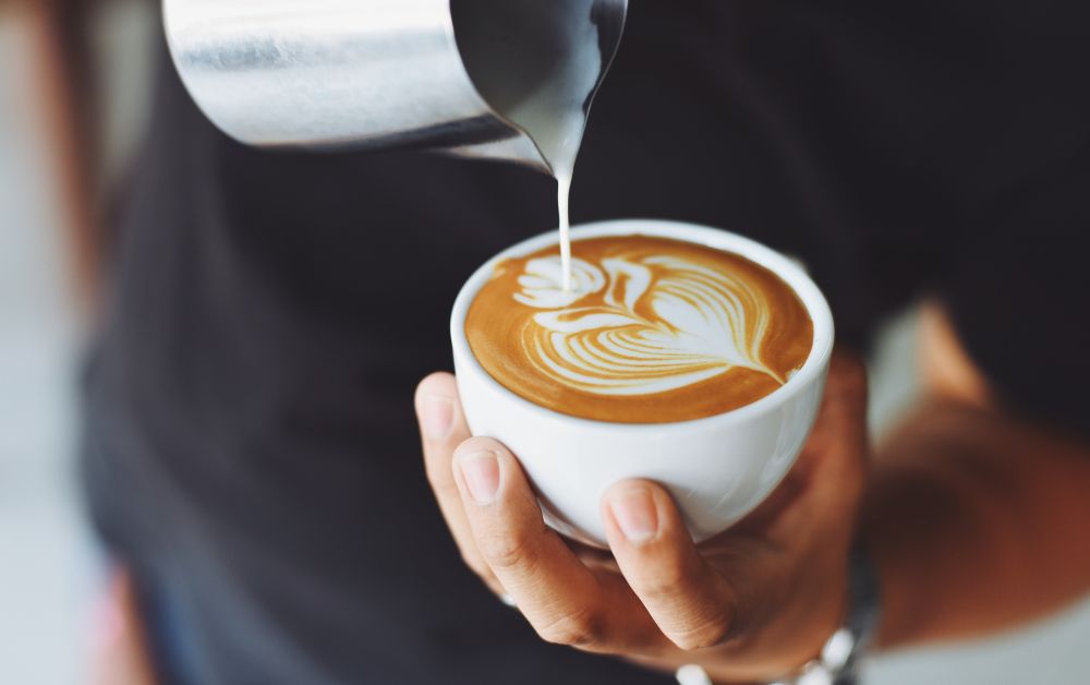 Guy holding a cup of coffee latte designing some arts on top using milk.
