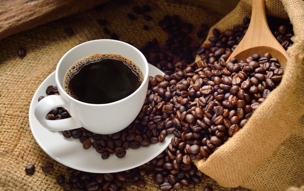 Black coffee served in a white mug next to a sack of raw coffee beans.