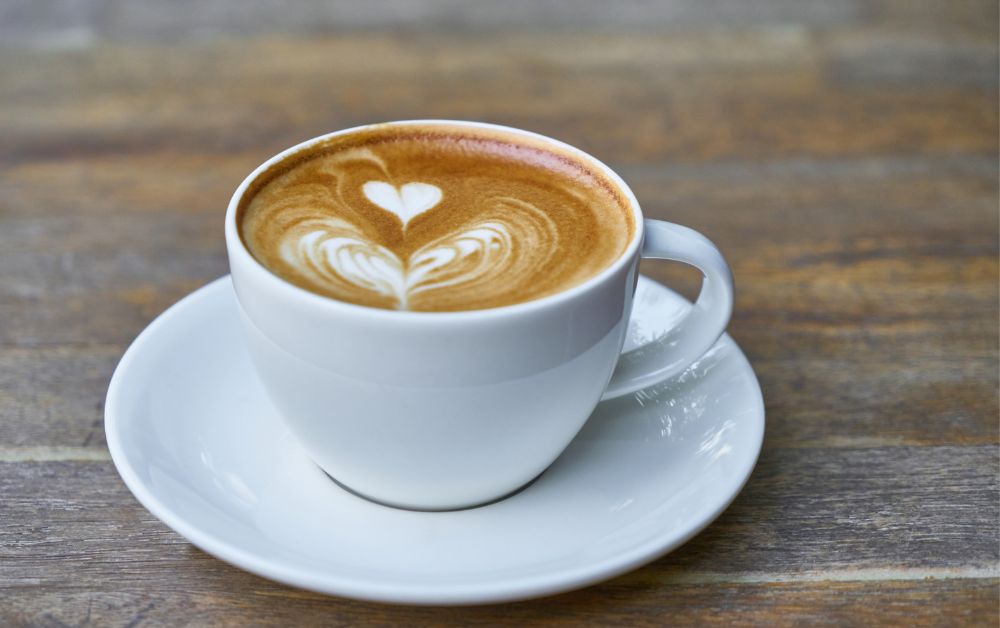 Coffee latte in a white mug sitting on a wooden table.